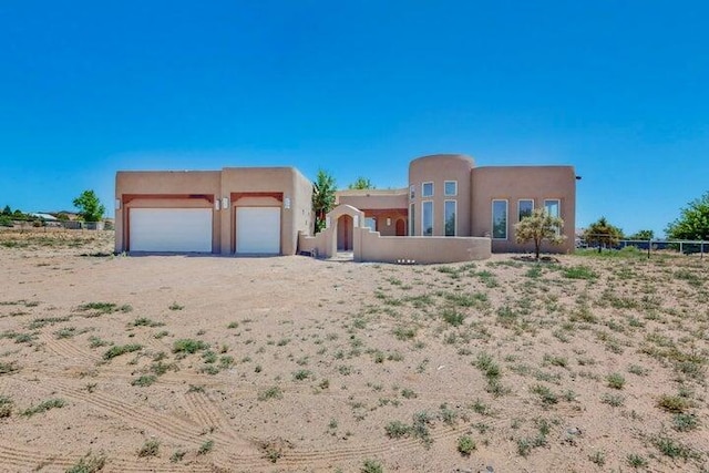 pueblo-style house featuring a garage, fence, and stucco siding