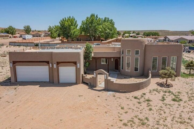 adobe home with a garage, dirt driveway, fence, and stucco siding