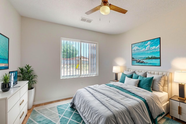 bedroom featuring light wood-style floors, baseboards, visible vents, and a textured ceiling