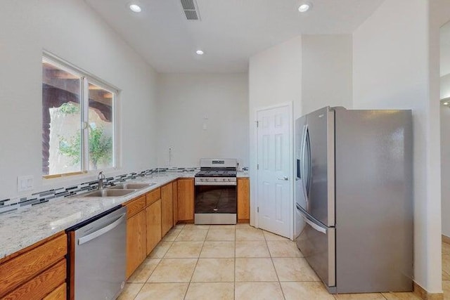 kitchen featuring light tile patterned flooring, recessed lighting, stainless steel appliances, a sink, and brown cabinetry