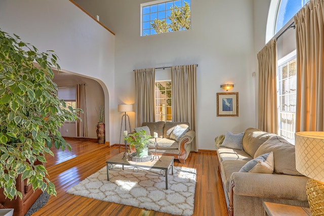 living room with arched walkways, hardwood / wood-style floors, plenty of natural light, and a towering ceiling