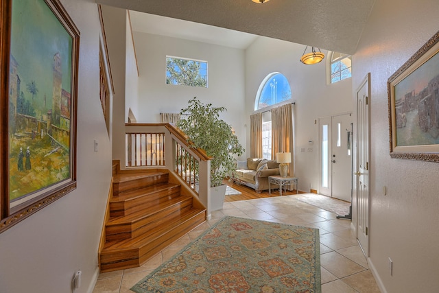 foyer entrance featuring baseboards, light tile patterned flooring, stairway, and a towering ceiling