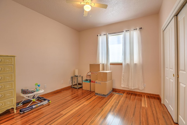 misc room featuring a textured ceiling, ceiling fan, light wood finished floors, and baseboards