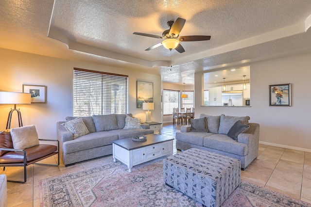 living area featuring a ceiling fan, a tray ceiling, a textured ceiling, and baseboards