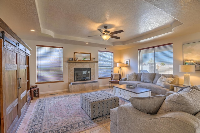 living area with light tile patterned floors, a barn door, a raised ceiling, a tile fireplace, and a healthy amount of sunlight