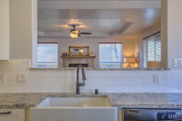 kitchen with a textured ceiling, a sink, dishwasher, a tray ceiling, and a tiled fireplace