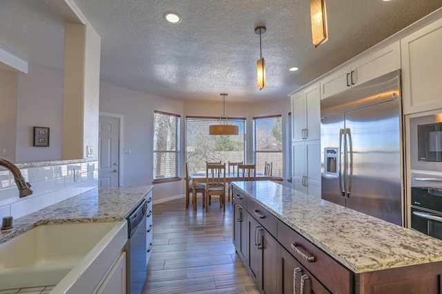 kitchen with built in appliances, a sink, white cabinets, backsplash, and light stone countertops