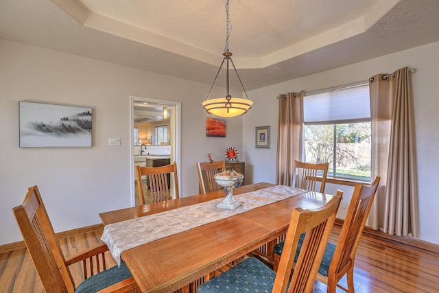 dining area featuring a textured ceiling, a tray ceiling, hardwood / wood-style floors, and baseboards