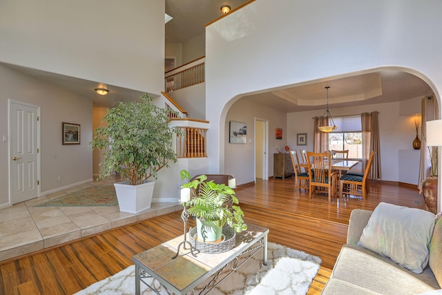 living area with stairs, arched walkways, a raised ceiling, and wood finished floors