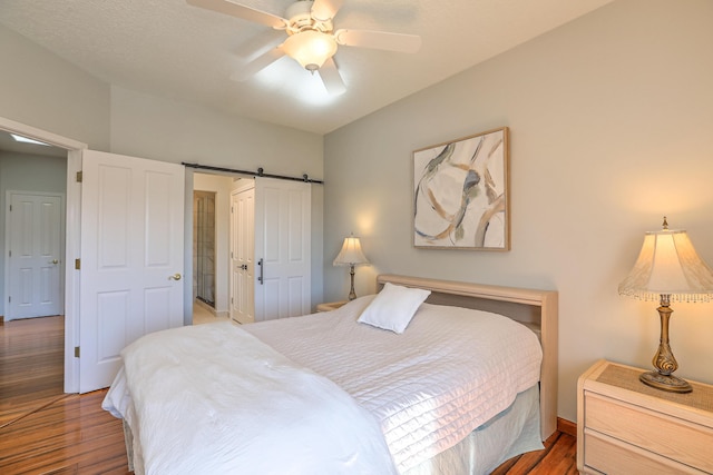 bedroom featuring ceiling fan, a barn door, and wood finished floors