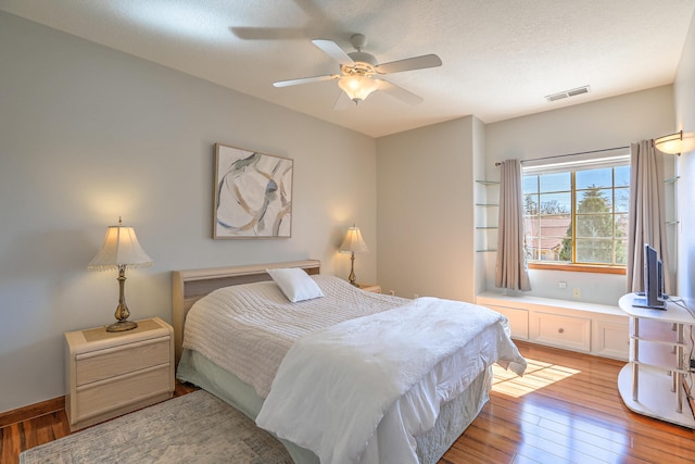 bedroom featuring light wood-style flooring, visible vents, ceiling fan, and a textured ceiling