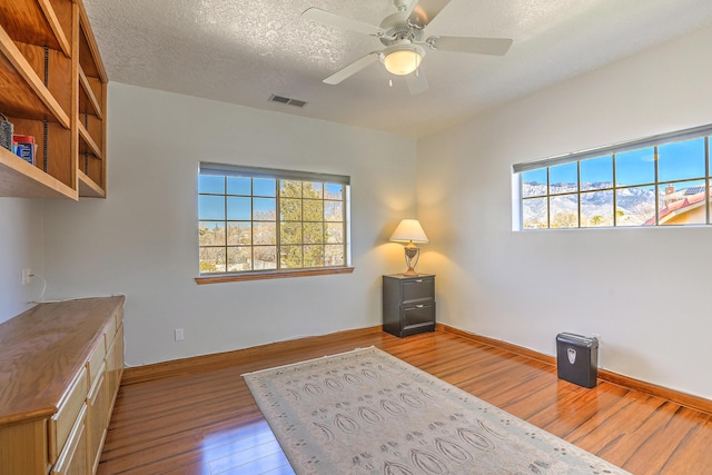 unfurnished office featuring baseboards, visible vents, a ceiling fan, hardwood / wood-style floors, and a textured ceiling