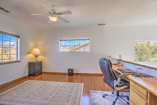 office area with a textured ceiling, wood-type flooring, visible vents, and baseboards