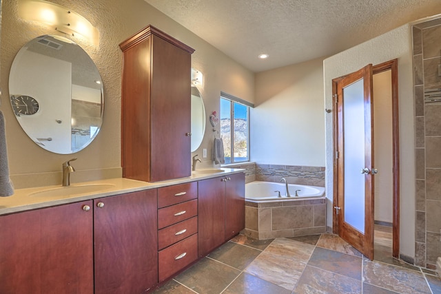 bathroom with a textured ceiling, double vanity, a sink, and a bath