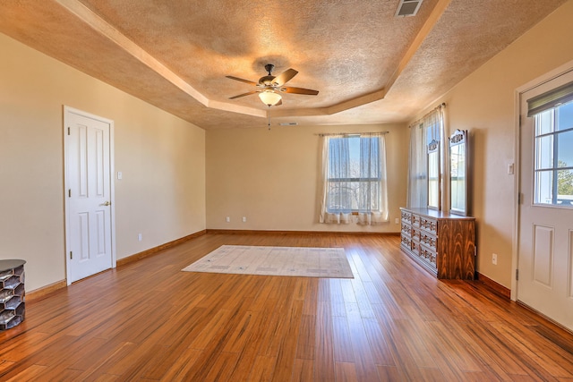 unfurnished room featuring a textured ceiling, wood finished floors, a raised ceiling, and visible vents