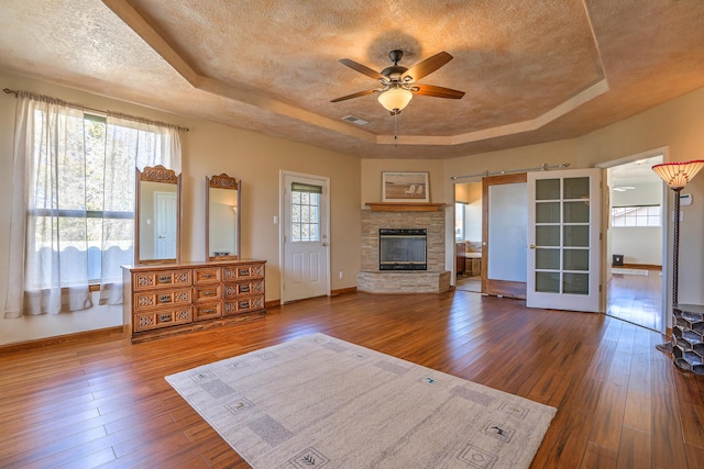 unfurnished living room featuring a textured ceiling, a barn door, hardwood / wood-style flooring, visible vents, and a raised ceiling