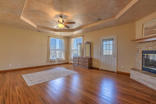 unfurnished living room with a textured ceiling, a fireplace, wood finished floors, visible vents, and a tray ceiling