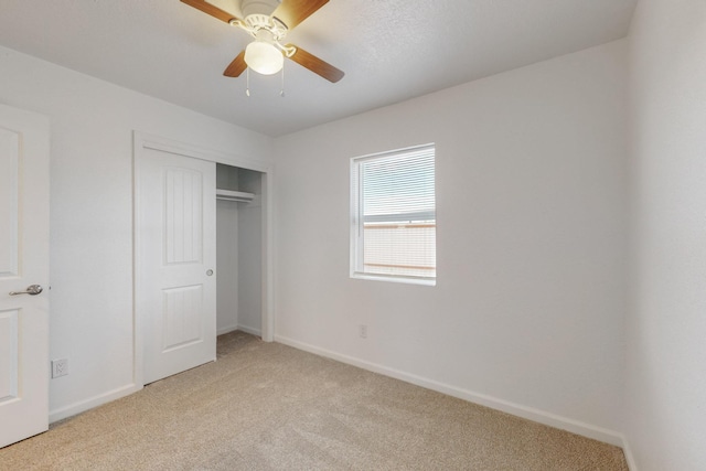 unfurnished bedroom featuring light carpet, a closet, baseboards, and a ceiling fan