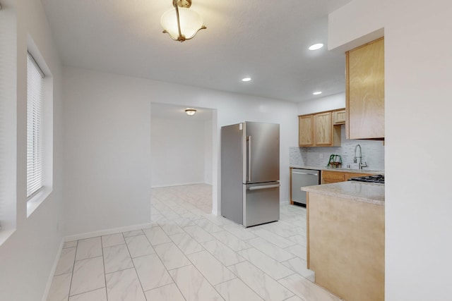 kitchen featuring backsplash, light brown cabinetry, light countertops, appliances with stainless steel finishes, and a sink