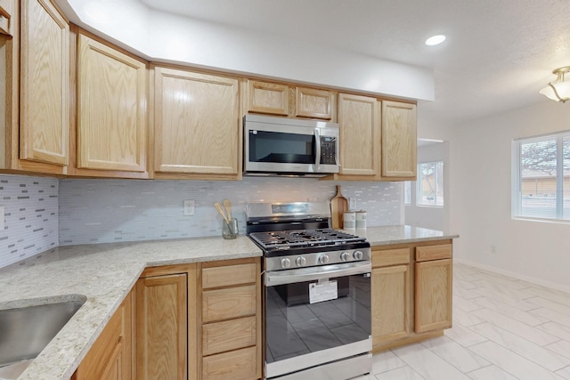 kitchen featuring tasteful backsplash, light brown cabinets, baseboards, light stone counters, and appliances with stainless steel finishes