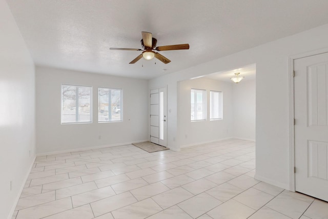 empty room featuring a textured ceiling, baseboards, and a ceiling fan