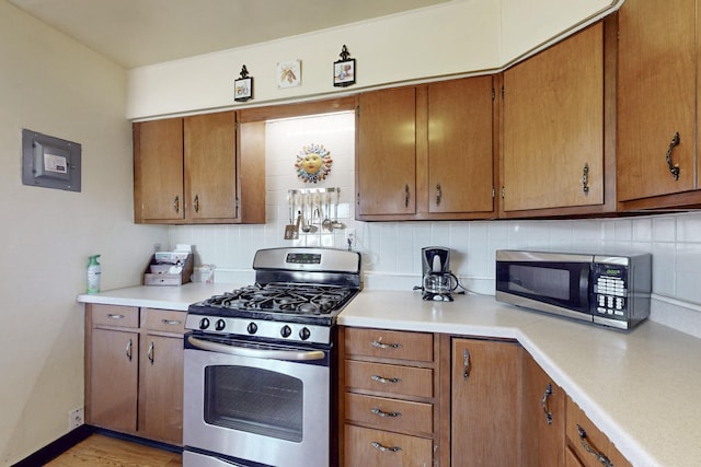 kitchen with stainless steel appliances, light countertops, backsplash, brown cabinetry, and electric panel