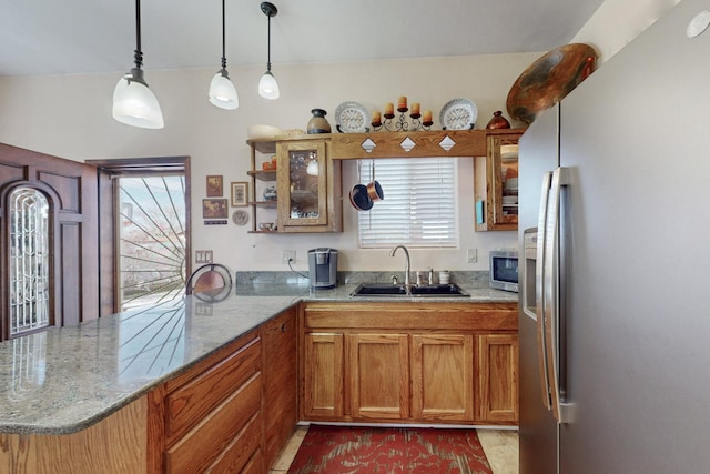 kitchen with light stone counters, stainless steel appliances, brown cabinetry, a sink, and a peninsula