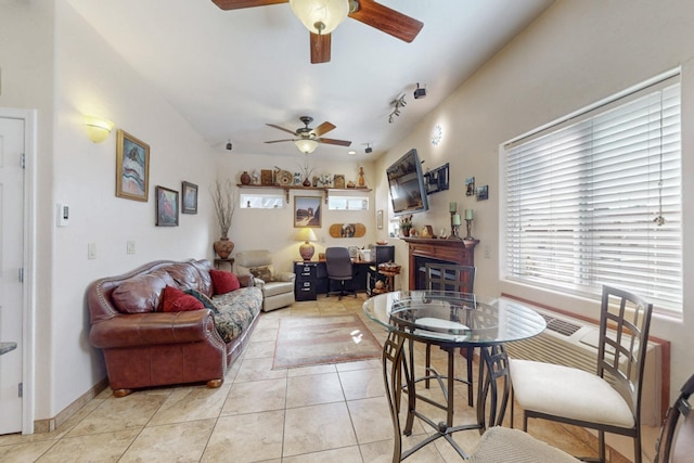 living area with a glass covered fireplace, light tile patterned flooring, ceiling fan, and baseboards