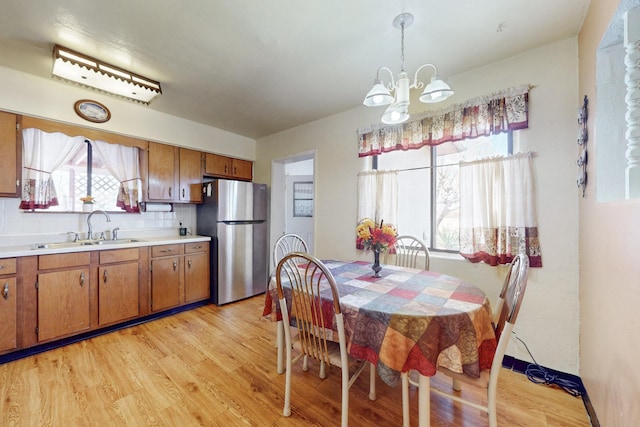 kitchen featuring brown cabinetry, light wood-style flooring, freestanding refrigerator, light countertops, and a sink