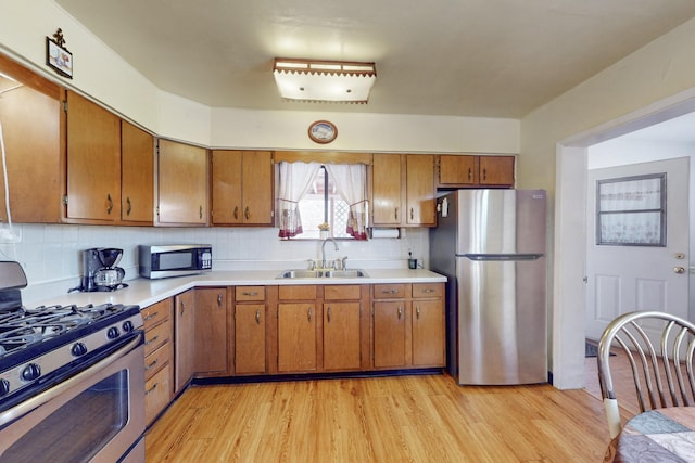 kitchen featuring brown cabinetry, stainless steel appliances, light countertops, light wood-type flooring, and a sink