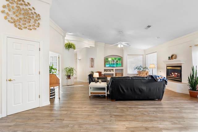 living area with visible vents, baseboards, light wood-type flooring, a fireplace, and a ceiling fan