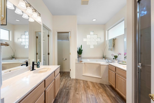 full bathroom with a garden tub, two vanities, wood finished floors, and a sink