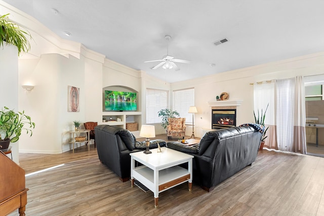 living room featuring visible vents, vaulted ceiling, wood finished floors, a glass covered fireplace, and a ceiling fan