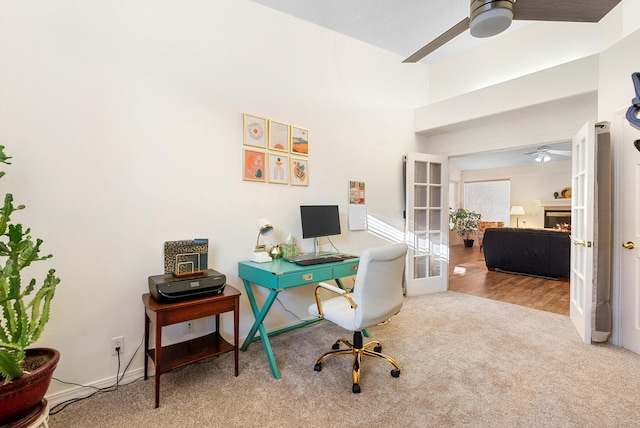 carpeted office space featuring a glass covered fireplace, french doors, and a ceiling fan