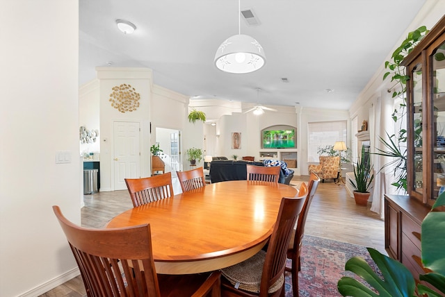 dining room featuring baseboards, visible vents, a fireplace, ceiling fan, and light wood-style floors