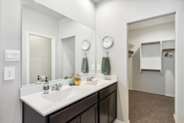 full bath with double vanity, a spacious closet, baseboards, and a sink