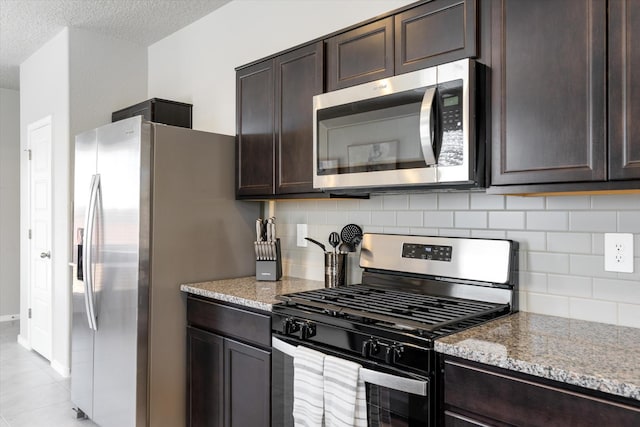 kitchen with dark brown cabinets, appliances with stainless steel finishes, light stone countertops, and decorative backsplash