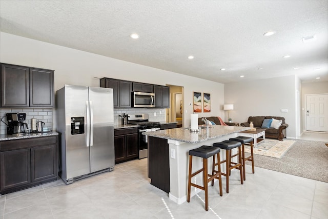 kitchen with a kitchen island with sink, stainless steel appliances, a breakfast bar, open floor plan, and light stone countertops