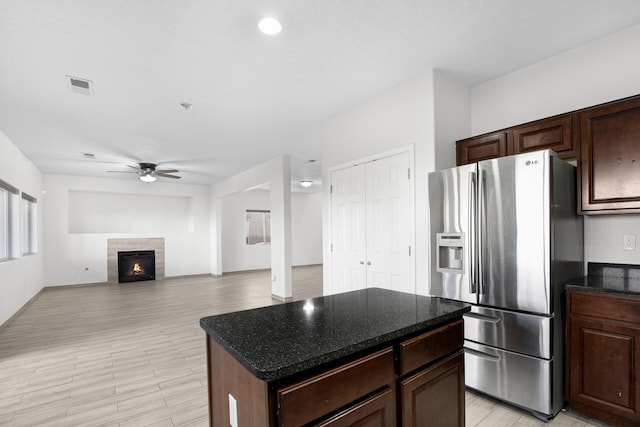 kitchen with a center island, stainless steel refrigerator with ice dispenser, visible vents, a ceiling fan, and a tile fireplace