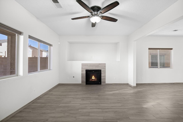 unfurnished living room with a textured ceiling, a tile fireplace, wood finished floors, and visible vents