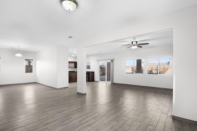 unfurnished living room with baseboards, visible vents, ceiling fan, dark wood-style flooring, and a textured ceiling