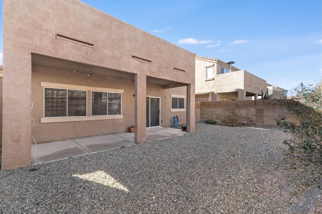 rear view of house featuring a patio area, fence, and stucco siding