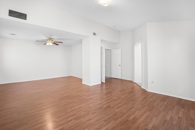 unfurnished room with arched walkways, visible vents, a textured ceiling, wood finished floors, and baseboards