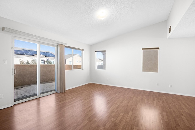 spare room featuring lofted ceiling, a textured ceiling, baseboards, and wood finished floors