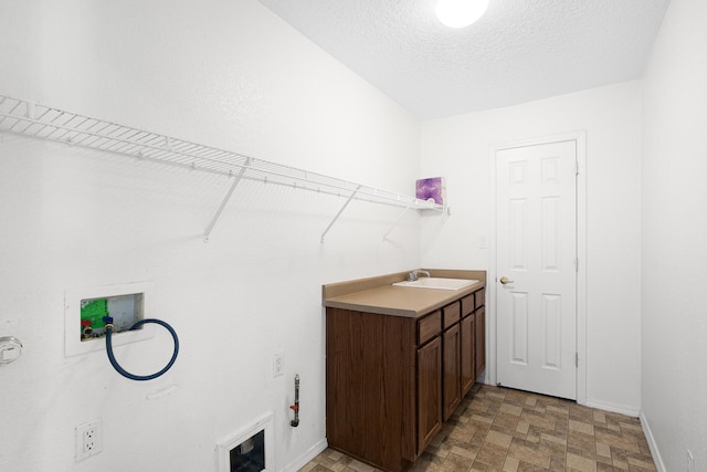 clothes washing area with cabinet space, baseboards, a textured ceiling, washer hookup, and a sink