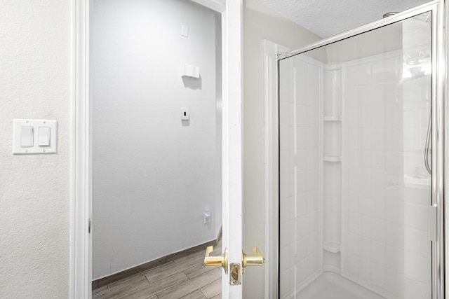 full bath with a textured wall, wood tiled floor, a shower stall, a textured ceiling, and baseboards