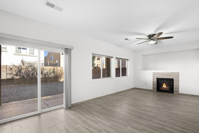 unfurnished living room with a tiled fireplace, wood finished floors, and visible vents