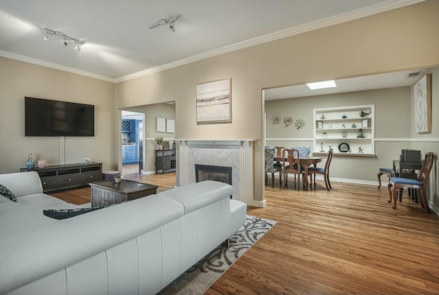 living room featuring built in shelves, a fireplace, visible vents, ornamental molding, and wood finished floors