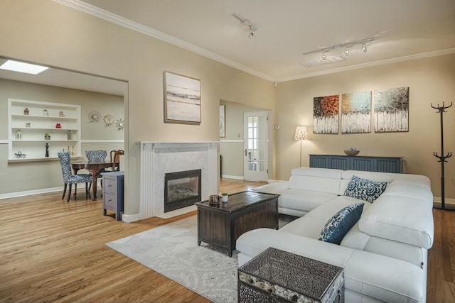 living room featuring baseboards, a premium fireplace, wood finished floors, crown molding, and built in shelves