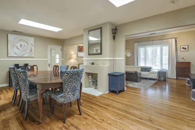 dining space featuring baseboards, a skylight, visible vents, and light wood-style floors